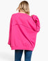 A woman viewed from behind wearing an oversized hot pink sweatshirt and blue jeans against a plain white background.