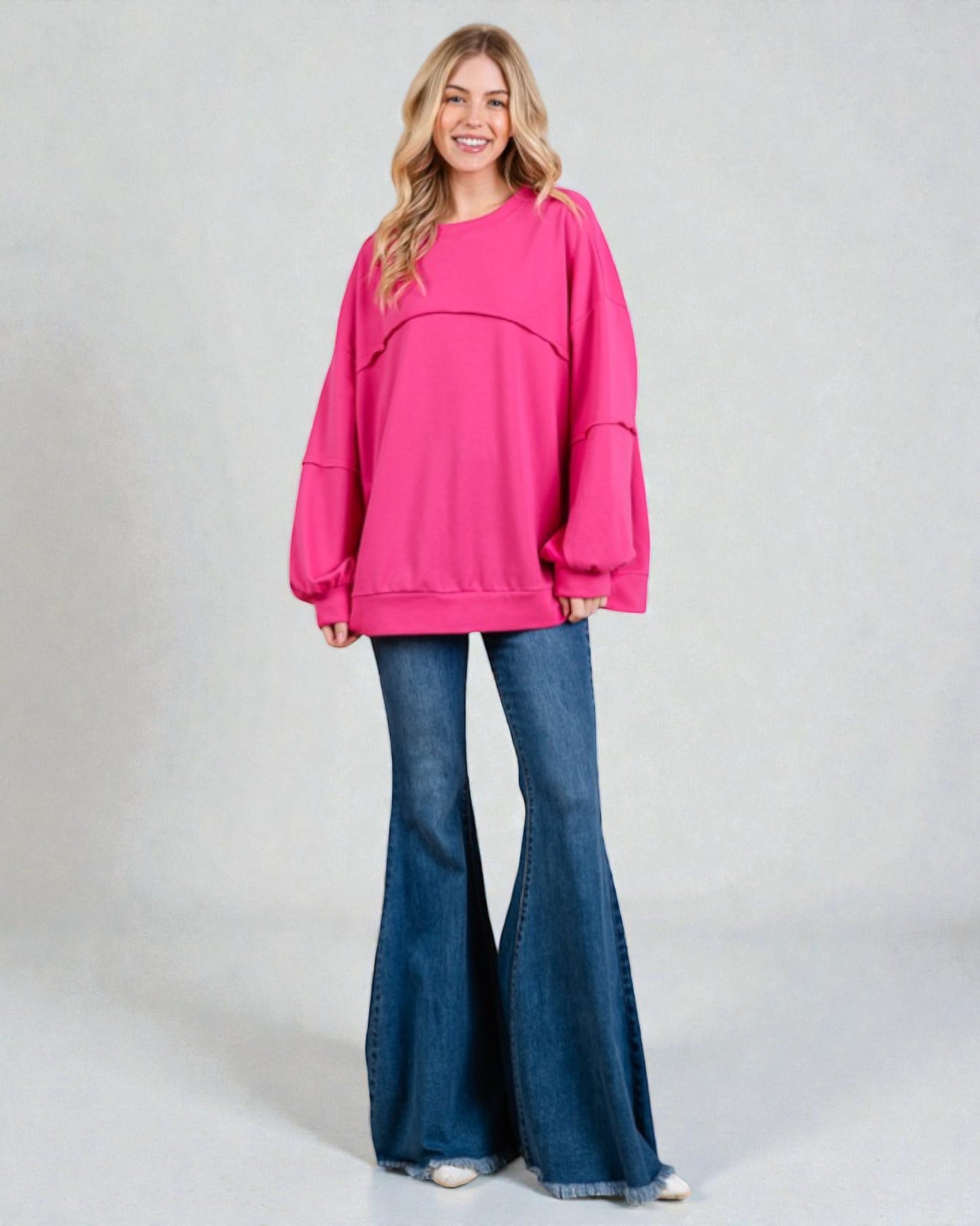 Woman wearing a bright pink sweatshirt and blue flared jeans on a plain background