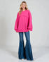 Woman wearing a bright pink sweatshirt and blue flared jeans on a plain background