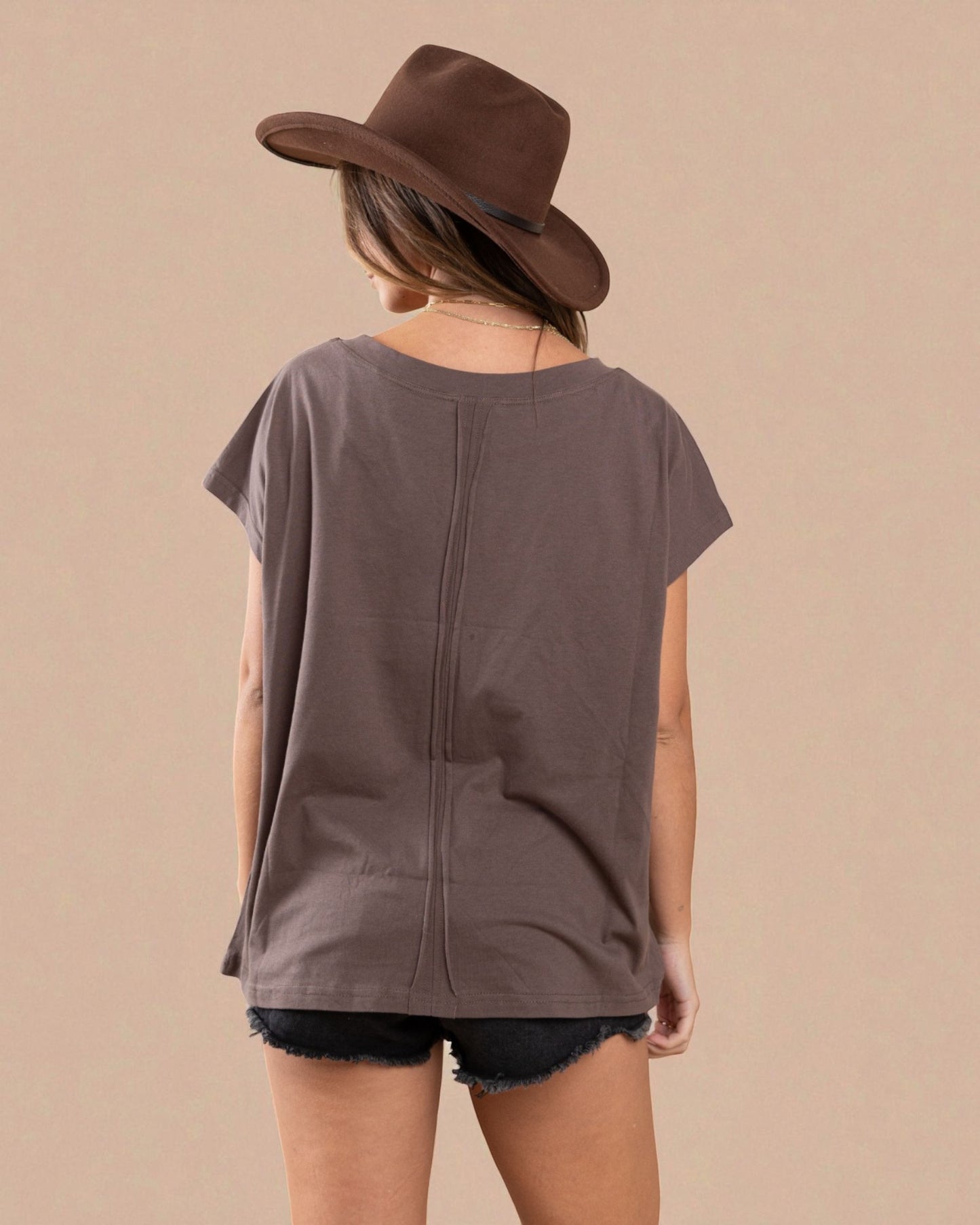 Person wearing a brown oversized t-shirt and cowboy hat on a beige background