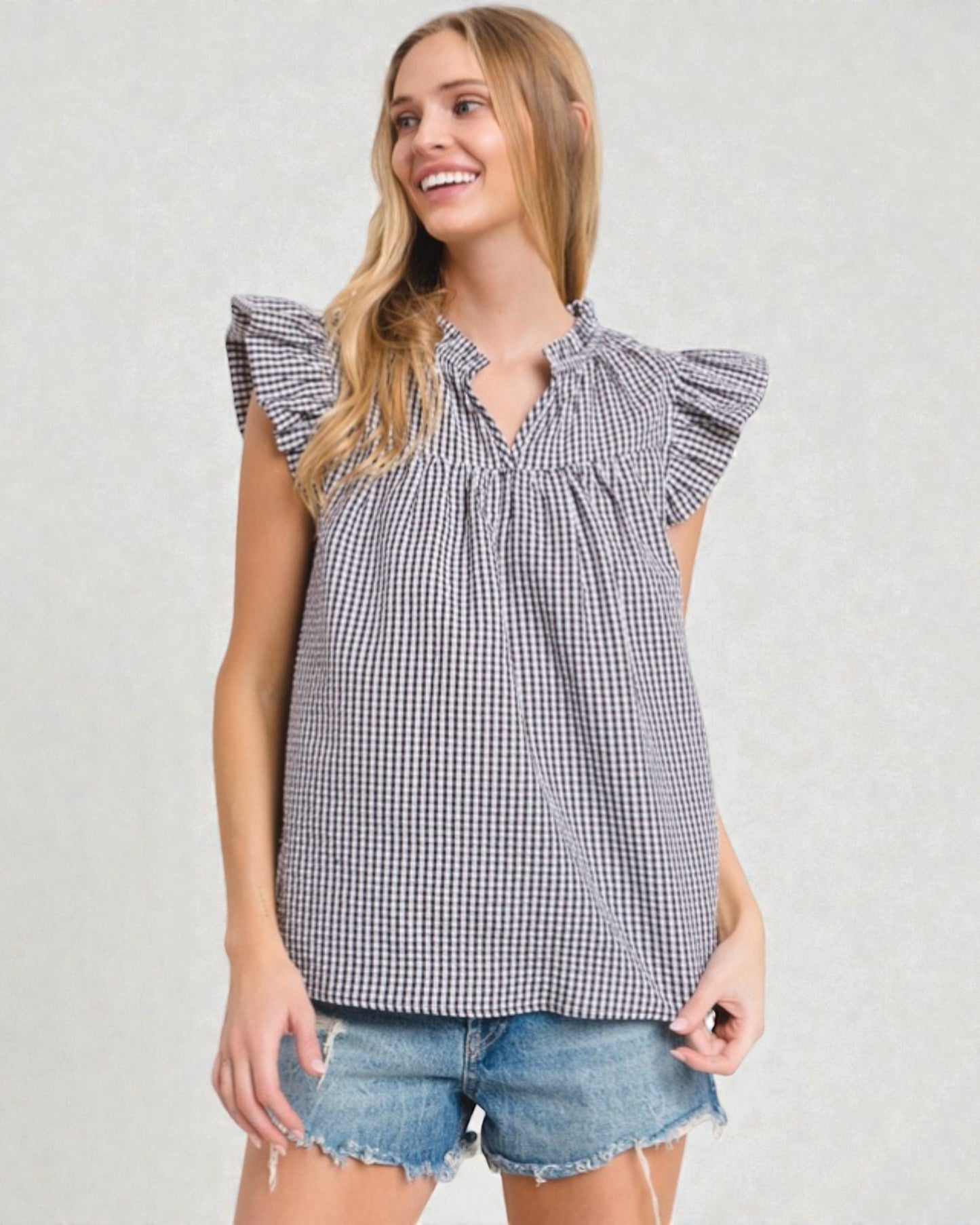 Woman wearing a checkered top with ruffled sleeves on a plain background