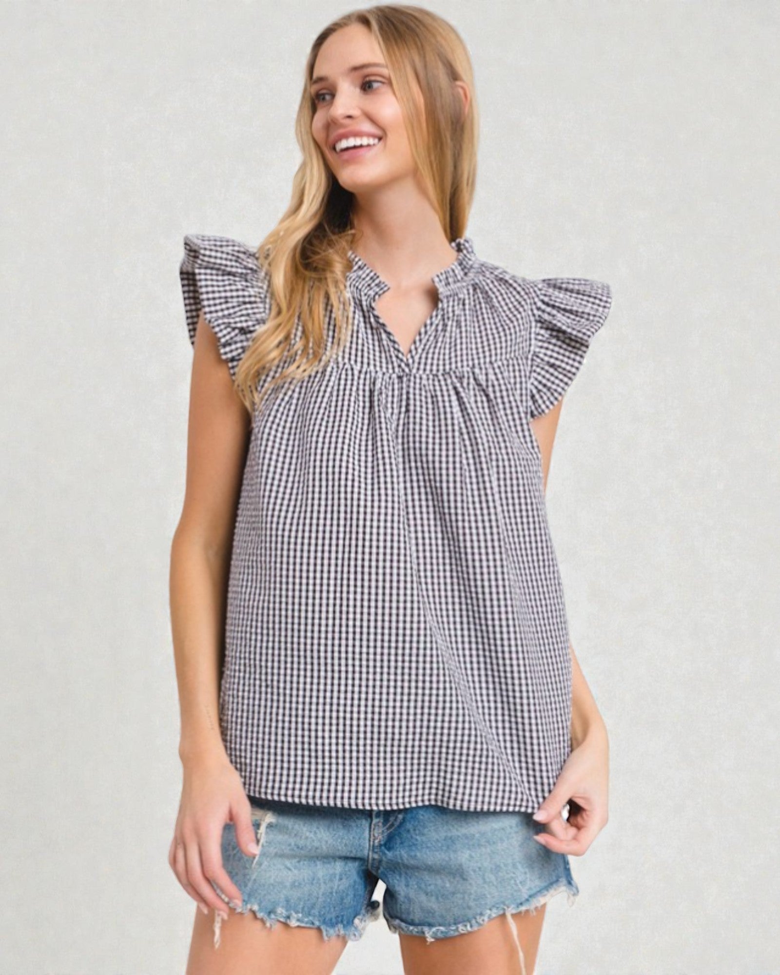 Woman wearing a checkered top with ruffled sleeves on a plain background