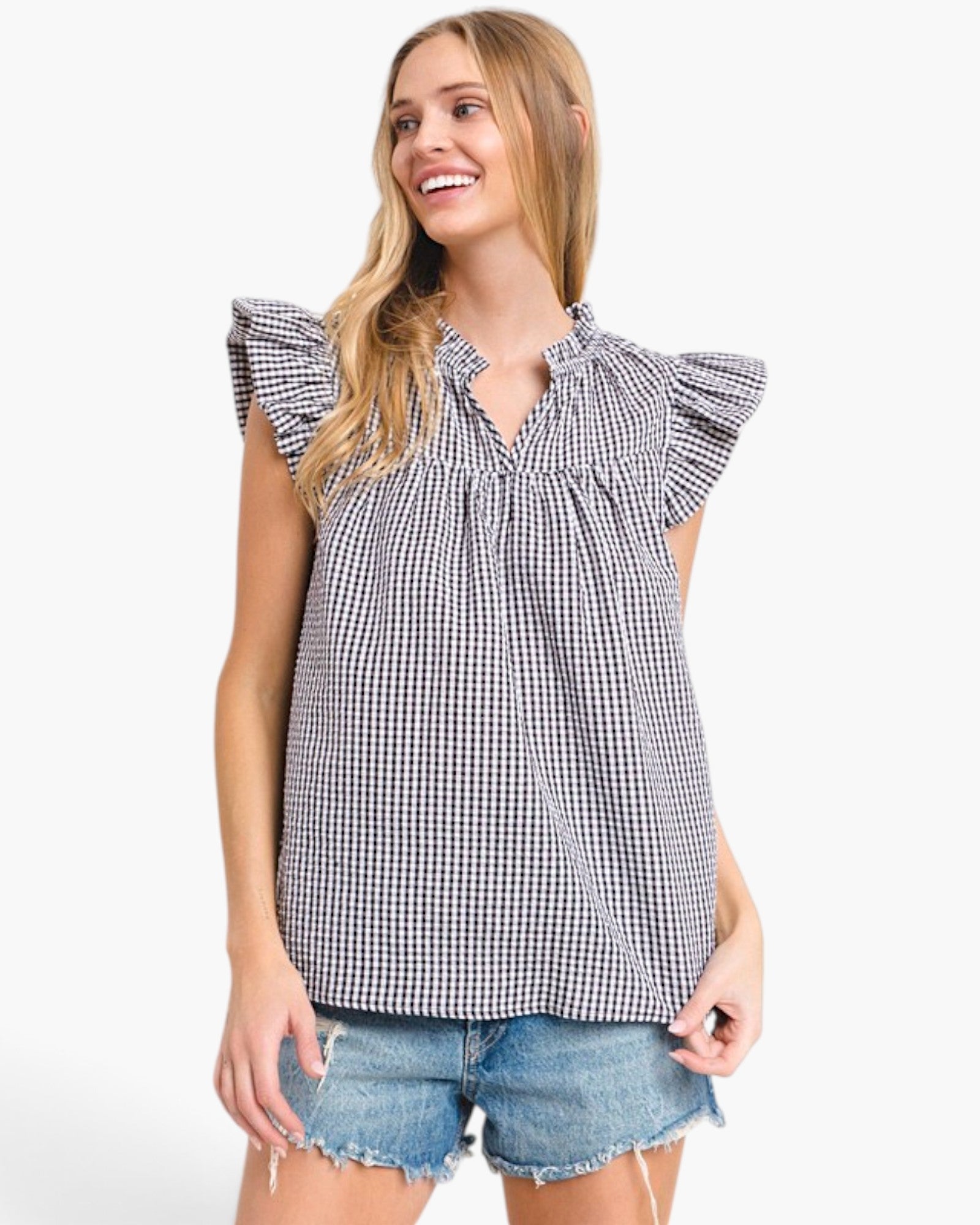 A woman wearing a black and white gingham check sleeveless blouse with ruffled cap sleeves and a smocked neckline, paired with denim shorts, against a plain white background.