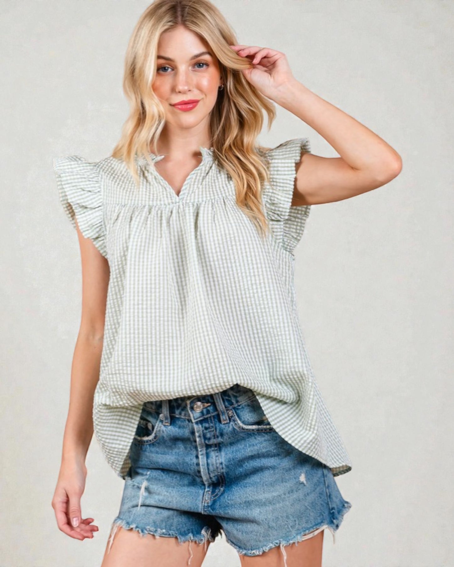 Woman wearing a light green checkered top and denim shorts on a plain background