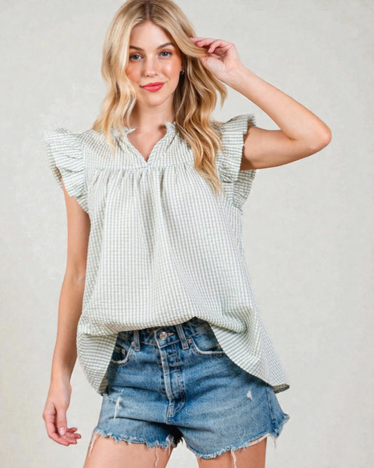 Woman wearing a light green checkered top and denim shorts on a plain background