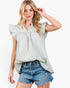 A woman modeling a light green and white gingham sleeveless blouse with ruffled cap sleeves and a smocked neckline, paired with distressed denim shorts against a plain white background.
