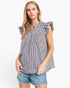 A woman modeling a sleeveless black and white gingham top with ruffled shoulder details and a smocked neckline, paired with denim shorts, against a plain white background.