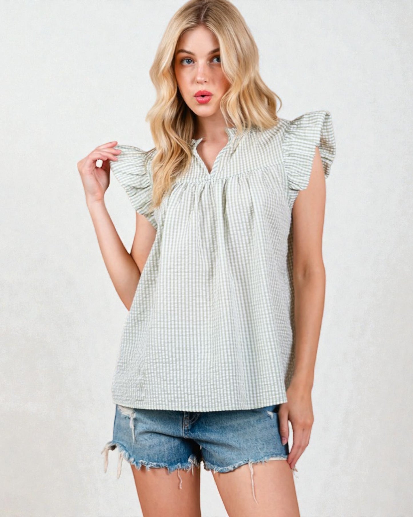 Woman wearing a light green checkered top and denim shorts on a white background