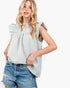A woman modeling a sleeveless, ruffled blouse with a green and white gingham pattern, paired with distressed denim shorts, against a plain white background.