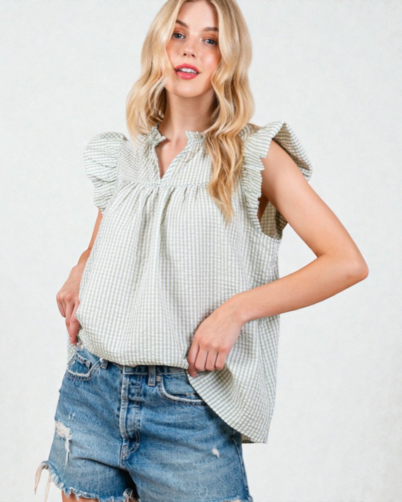 Woman wearing a light green checkered top with ruffled sleeves and denim shorts on a white background