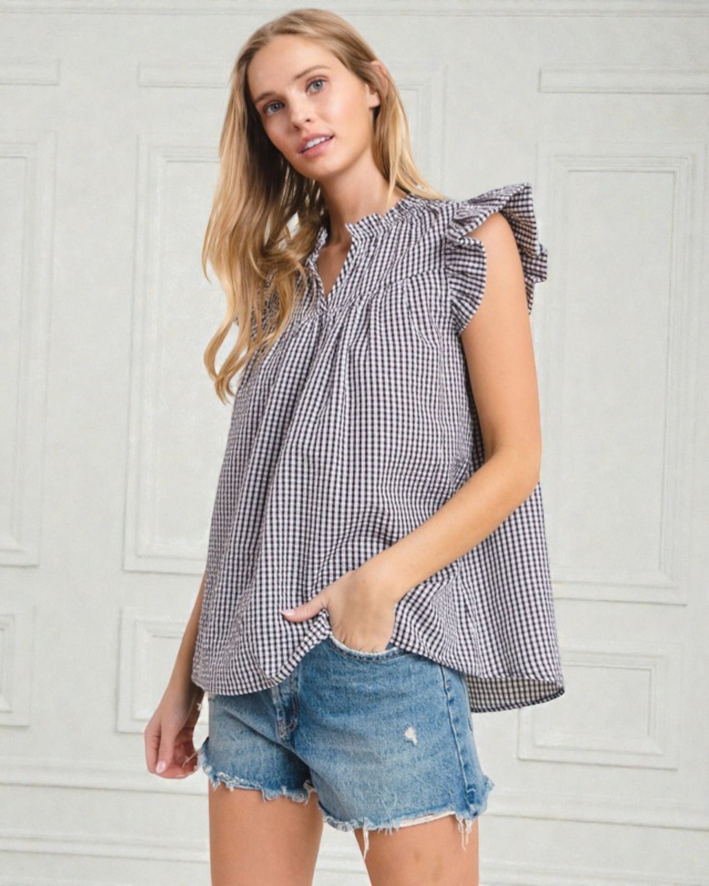 Woman wearing a checkered top and denim shorts against a white wall