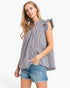 A woman modeling a sleeveless black and white gingham blouse with ruffled shoulders and a smocked neckline, paired with denim shorts, against a plain white studio background.