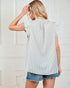 Woman wearing a light blue checkered top and denim shorts against a white wall.