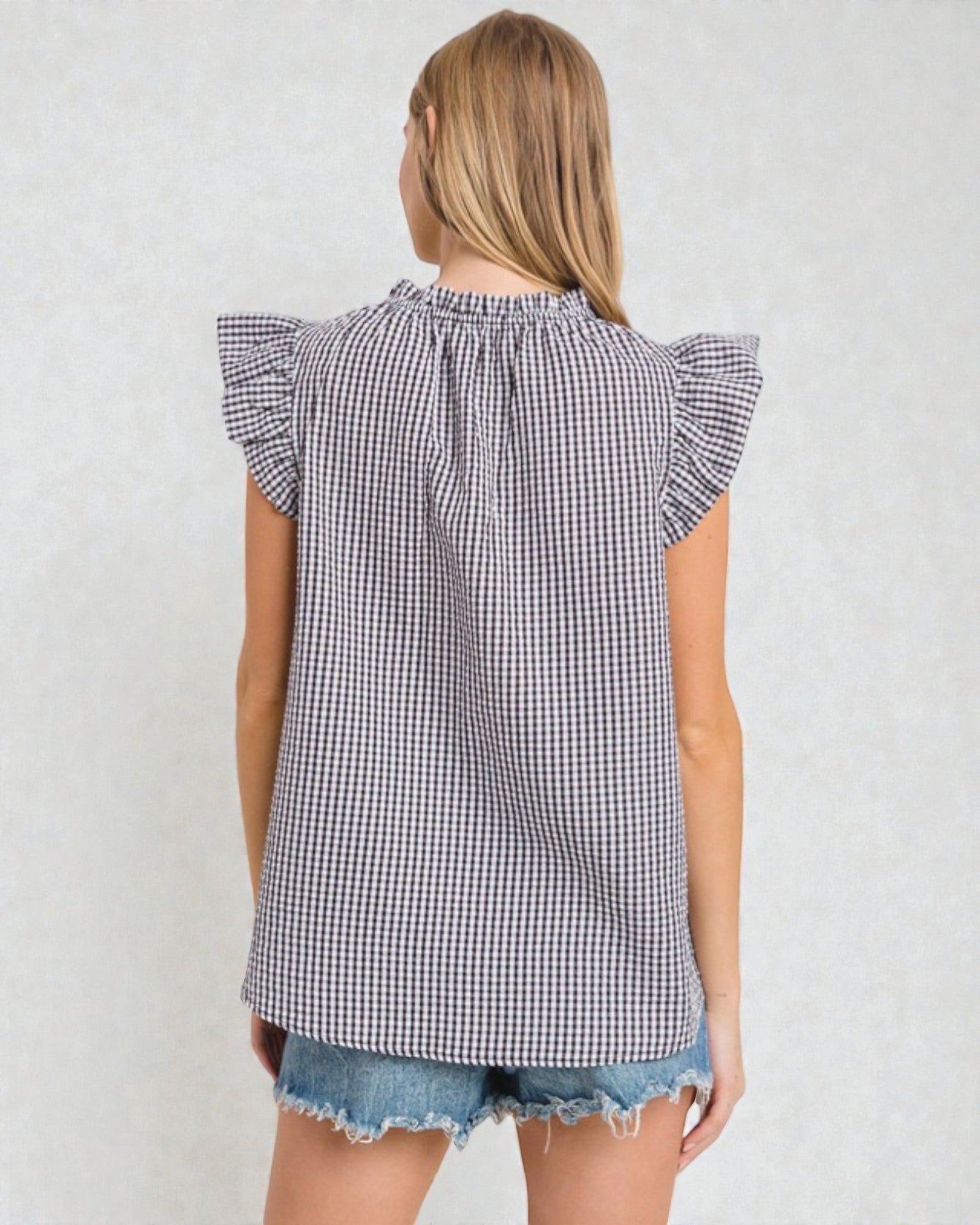 Woman wearing a black and white checkered top with ruffled sleeves on a plain background