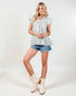 Woman wearing a light blue checkered blouse, denim shorts, and white boots on a white background