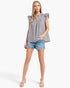 A woman modeling a sleeveless black and white gingham top with ruffled cap sleeves, paired with denim shorts and beige sandals, against a plain white studio background.