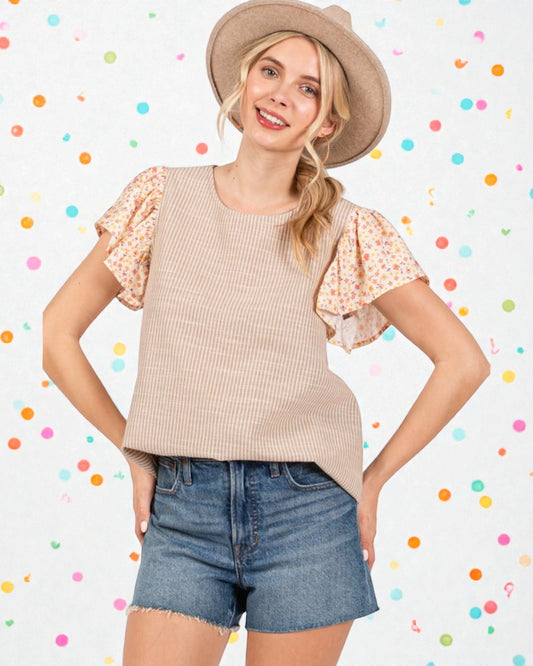 Woman wearing a beige top with floral sleeves, denim shorts, and a hat on a polka dot background