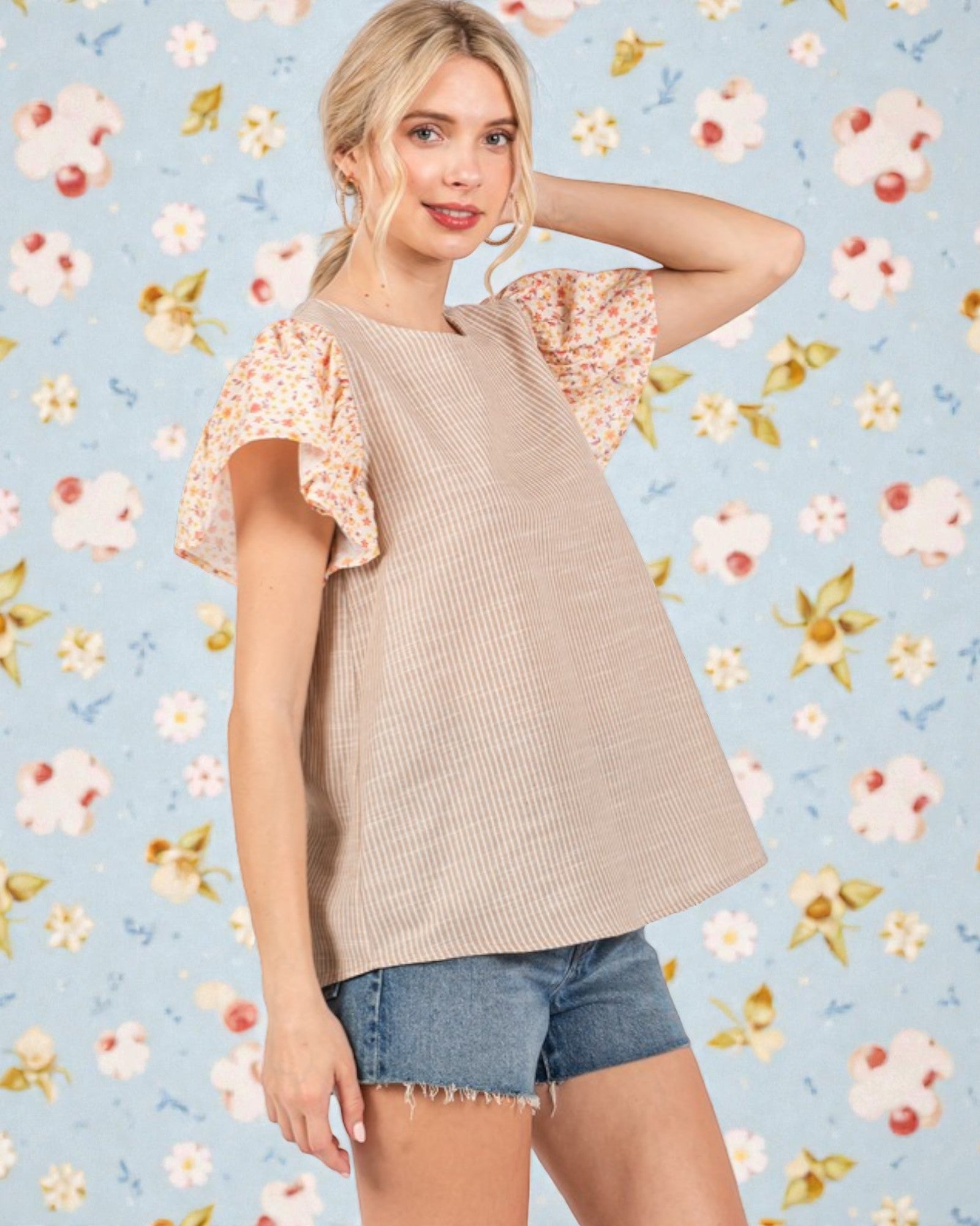 Woman wearing a beige top with floral sleeves against a floral-patterned background