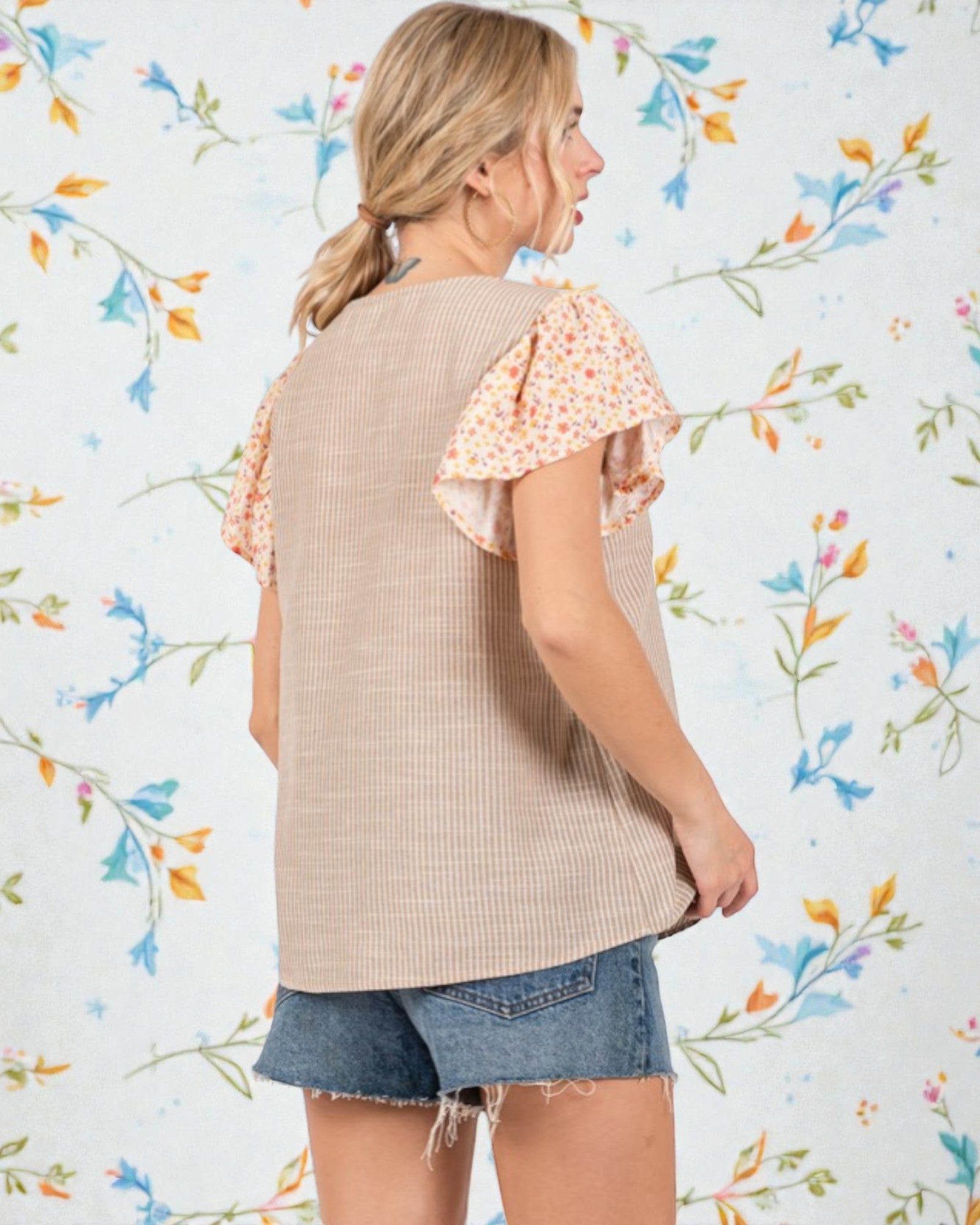 Woman wearing a beige knit top with floral sleeves against a floral-patterned background