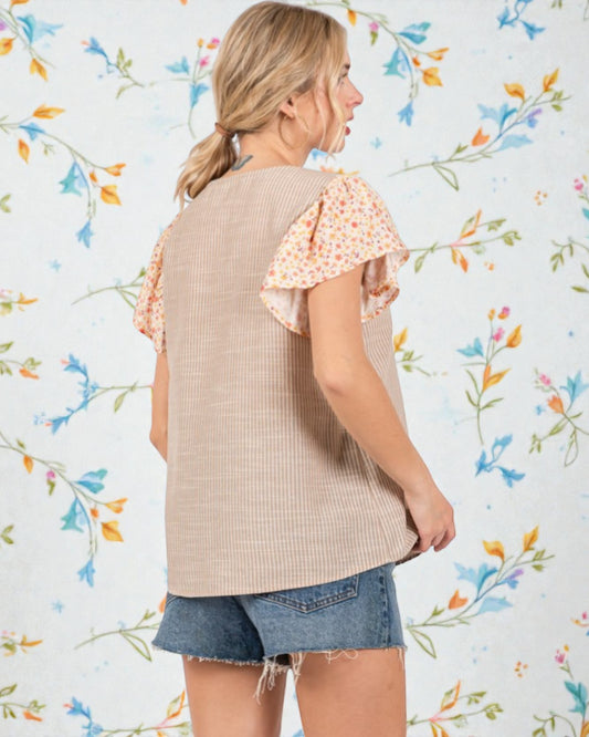 Woman wearing a beige knit top with floral sleeves against a floral-patterned background