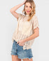 A woman modeling a cream-colored, short-sleeve crochet knit top with a large front patch pocket, paired with distressed denim shorts, against a light gray studio background.