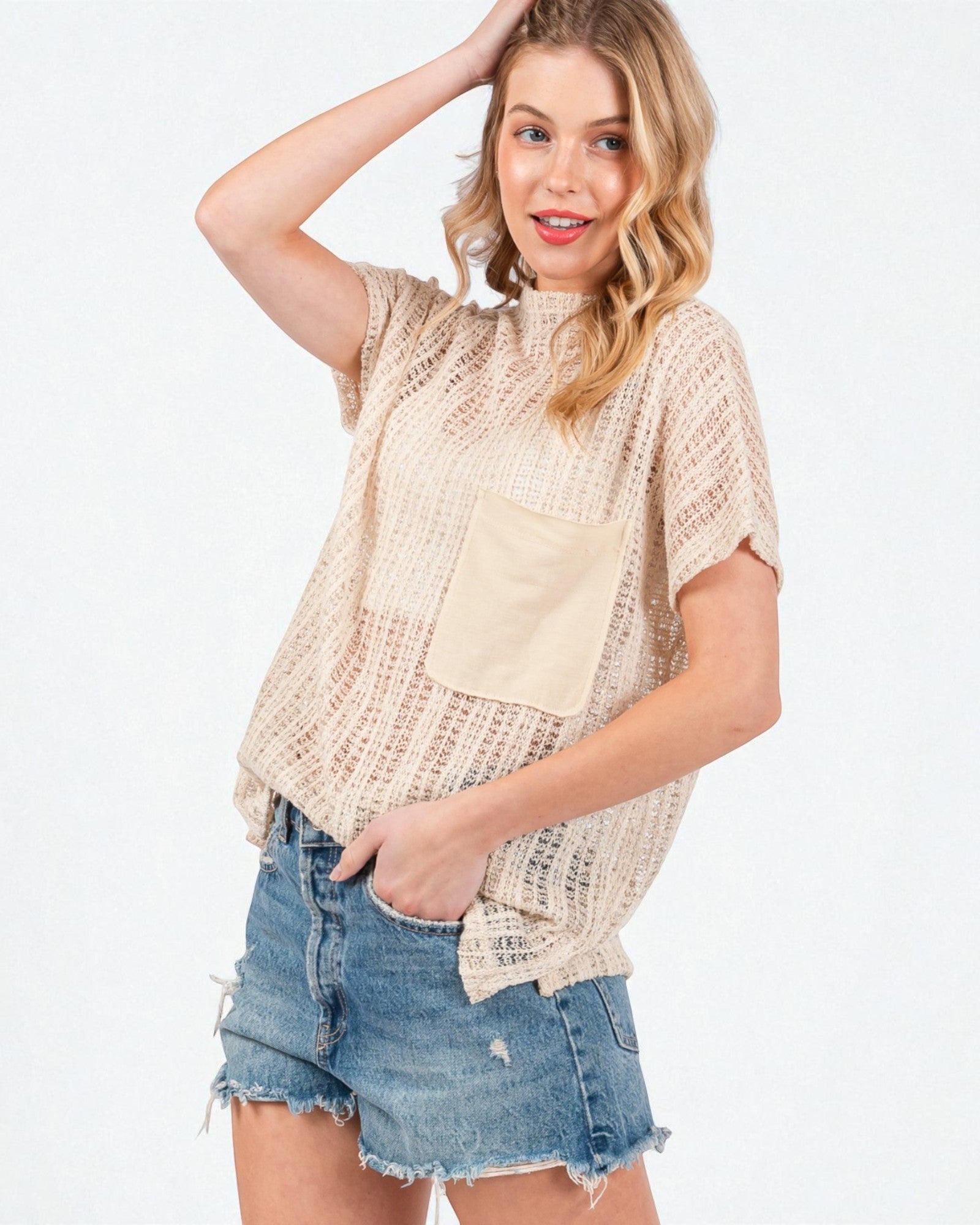 Woman wearing a beige crochet top with a pocket and denim shorts on a white background