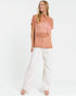Woman wearing a rust-colored top and white pants on a white background