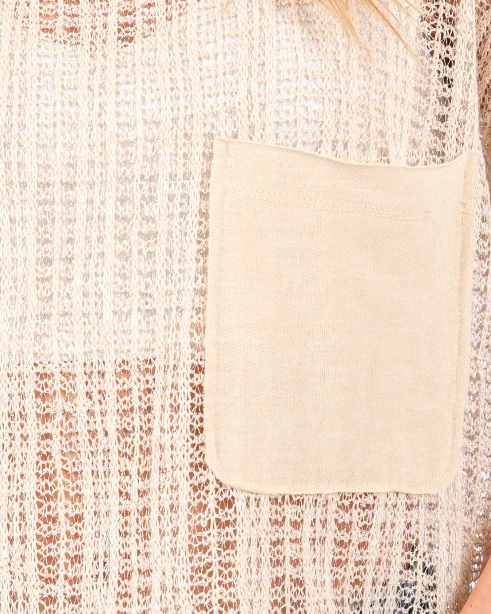 Close-up of a cream-colored knit top featuring a solid fabric chest pocket and a textured open-knit pattern.
