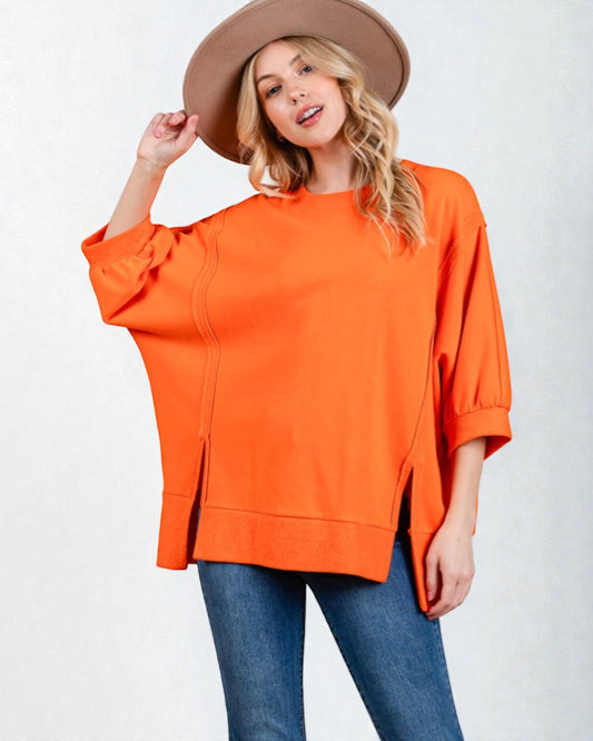 Woman wearing an orange oversized top and blue jeans with a beige hat on a white background