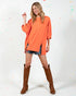 Woman wearing an orange oversized sweater and brown knee-high boots on a white background with colorful polka dots.