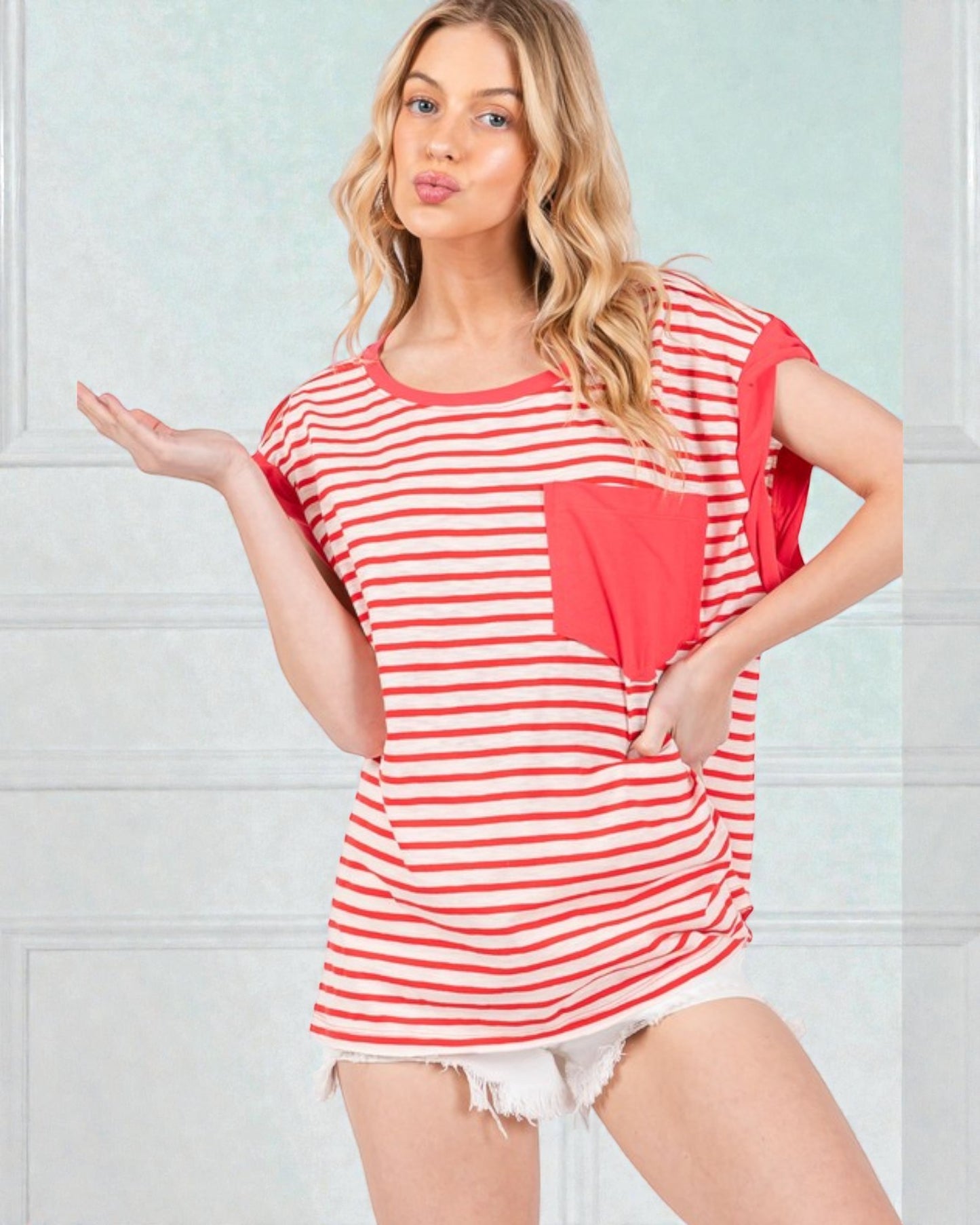 Woman wearing a red and white striped shirt with a heart design against a light blue wall.