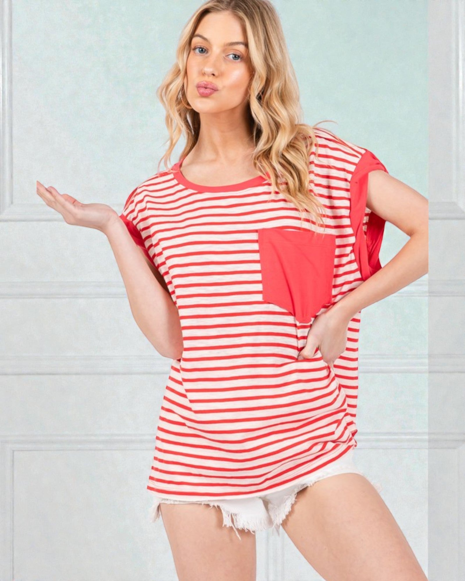 Woman wearing a red and white striped shirt with a heart design against a light blue wall.