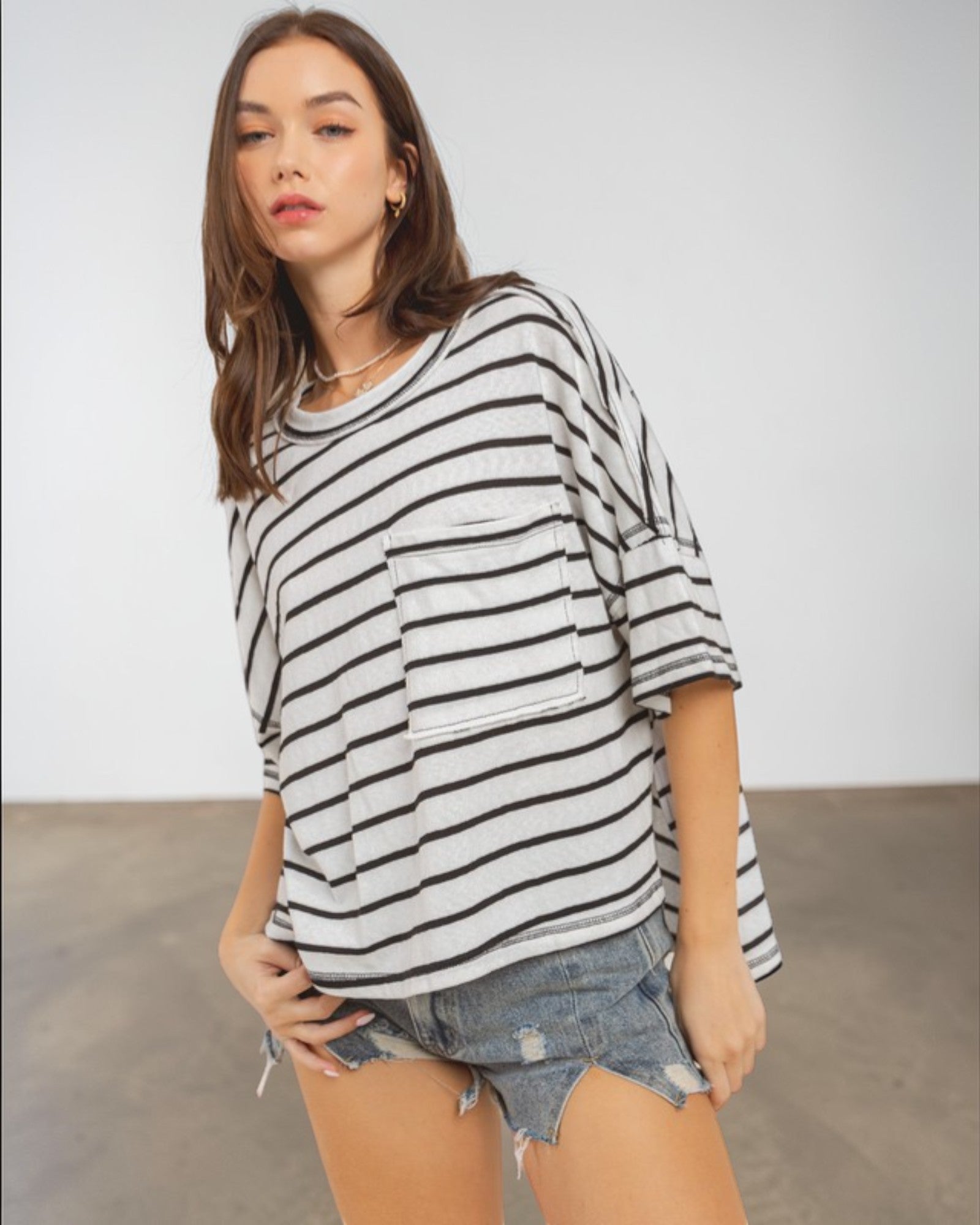 Woman wearing a black and white striped shirt and denim shorts against a plain background