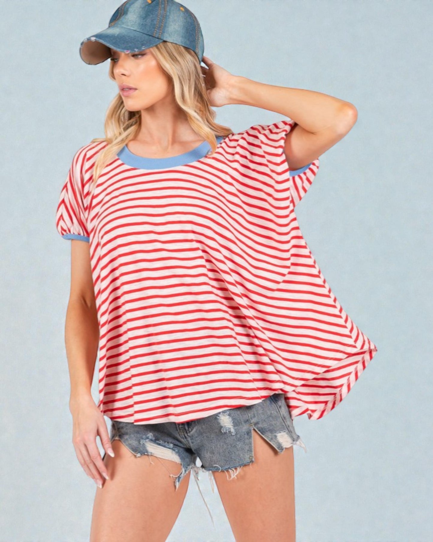 Woman wearing a red and white striped shirt, denim shorts, and a denim cap on a light blue background