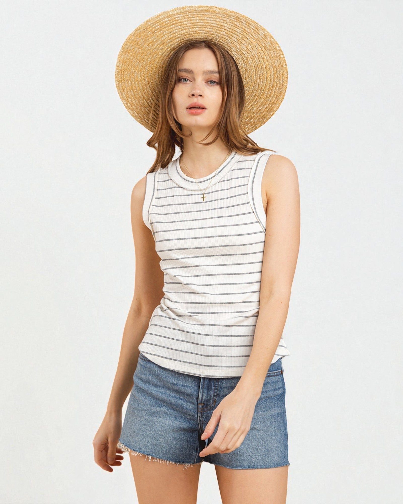 Woman wearing a striped tank top, denim shorts, and a straw hat on a white background