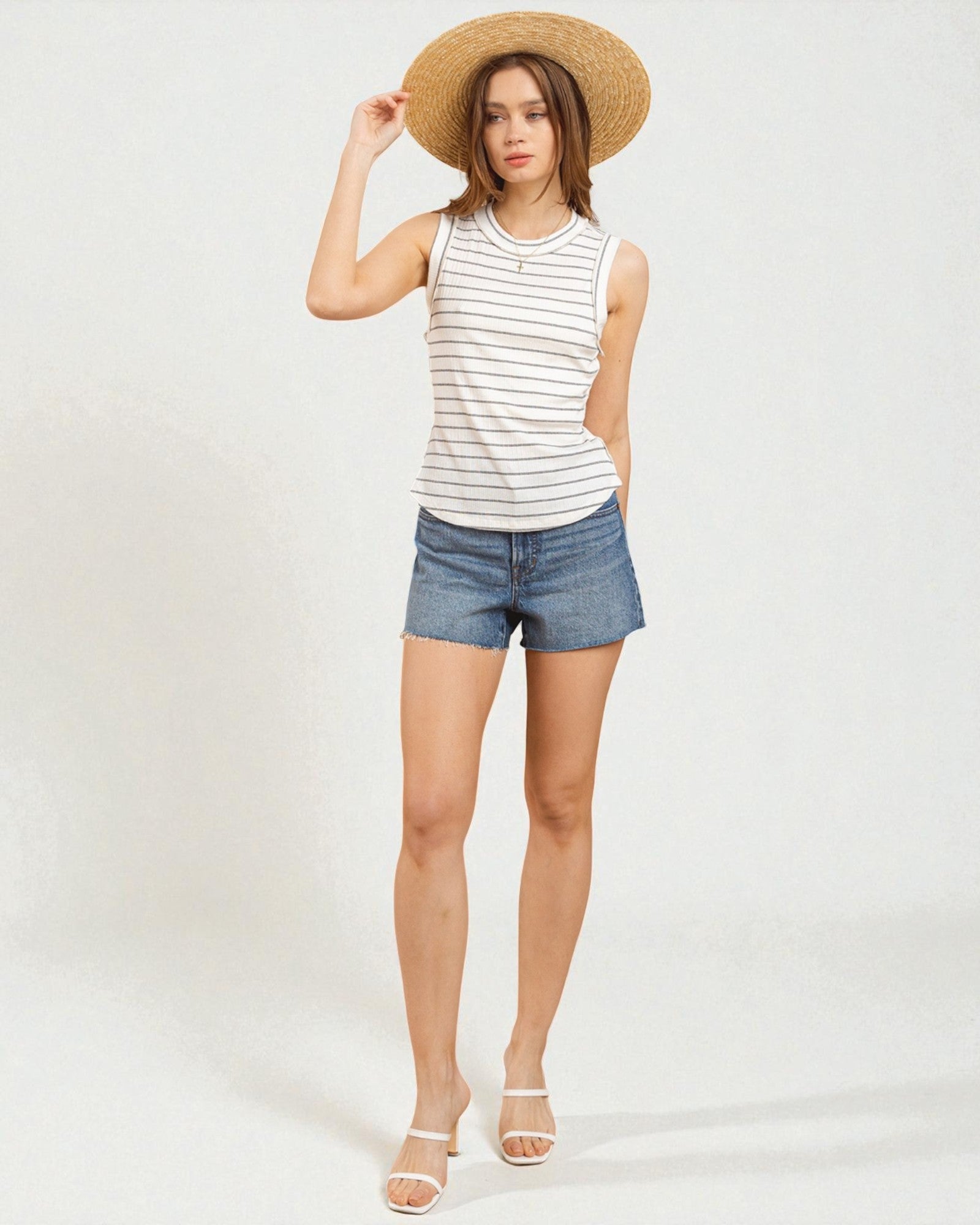 Woman wearing a striped tank top, denim shorts, and a straw hat on a white background