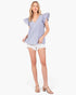 A woman modeling a light blue and white vertically striped ruffled sleeve top with white denim shorts and beige sandals, set against a plain white studio background.