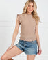 Woman wearing a beige sleeveless top and denim shorts against a white background