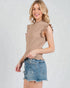 Woman wearing a brown textured top and denim shorts on a light gray background