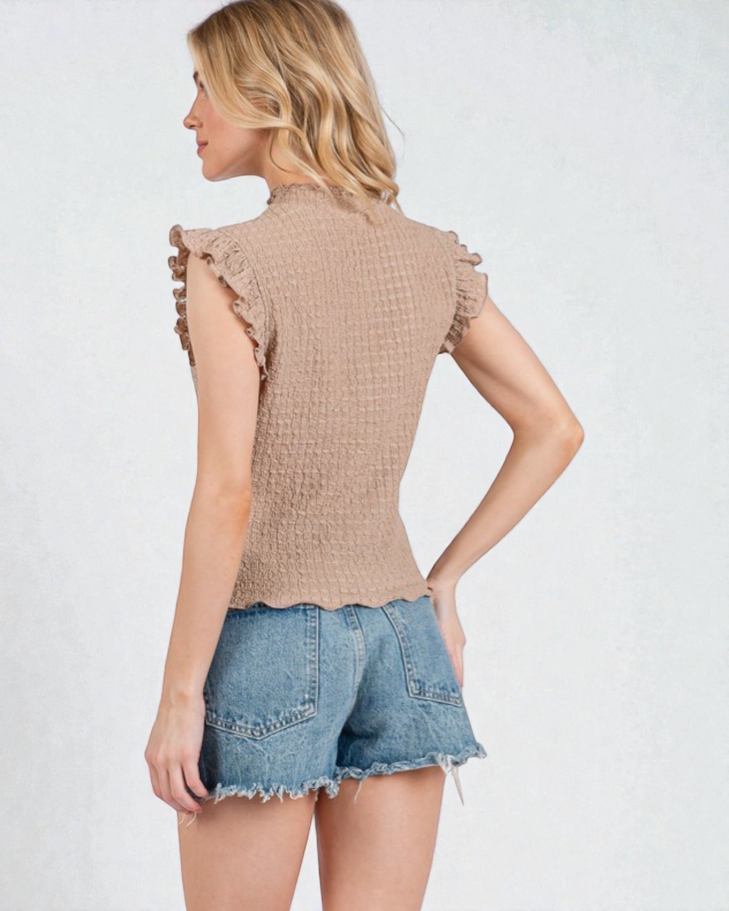 Woman wearing a beige textured top and denim shorts on a light gray background