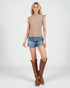 Woman wearing a beige top, denim shorts, and brown knee-high boots on a white background