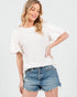 Woman wearing a white oversized t-shirt and denim shorts on a plain background