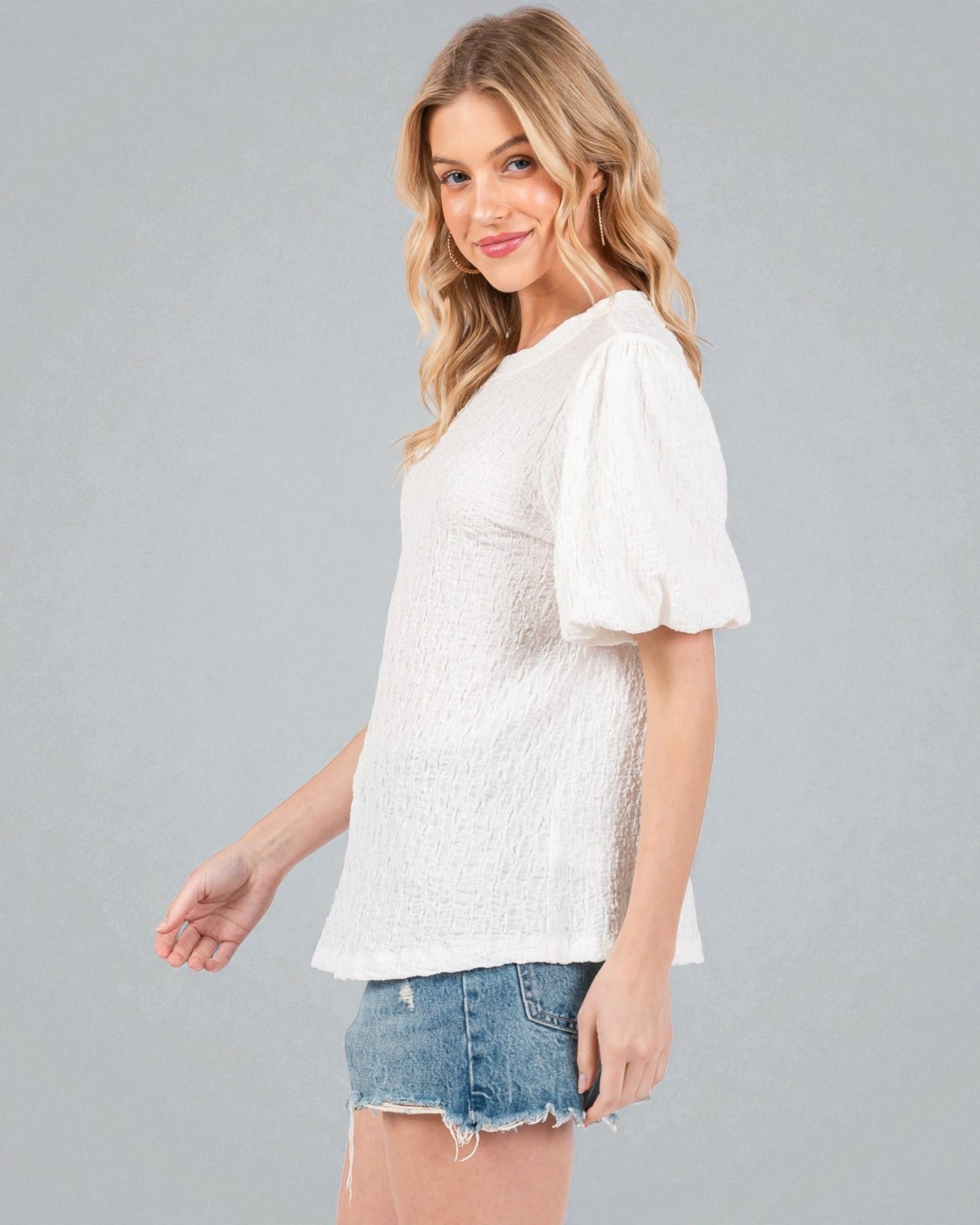 Woman wearing a white blouse with ruffled sleeves and denim shorts on a gray background