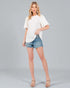 Woman wearing a white blouse and denim shorts on a gray background
