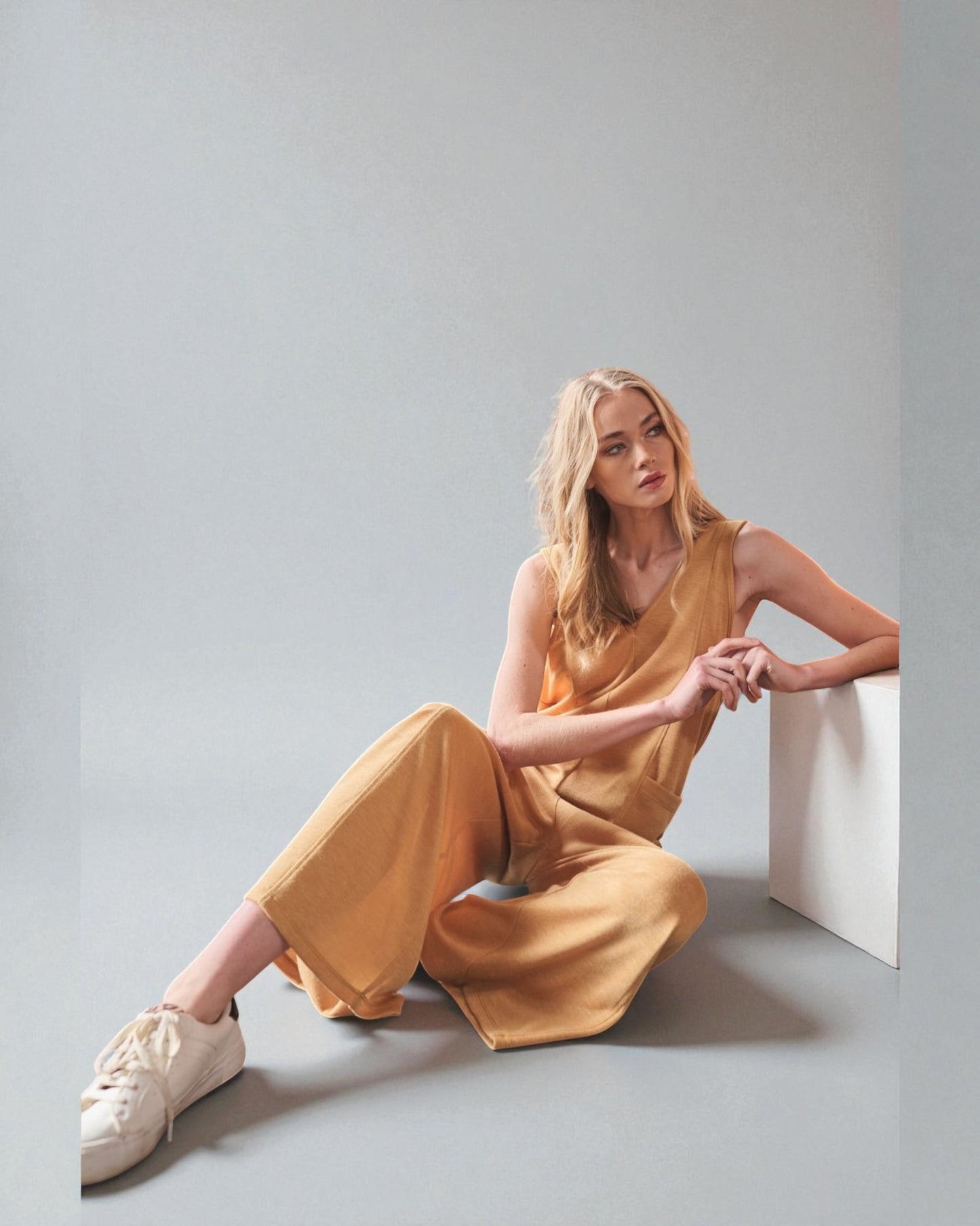 Woman in a yellow outfit sitting on a white surface against a light gray background