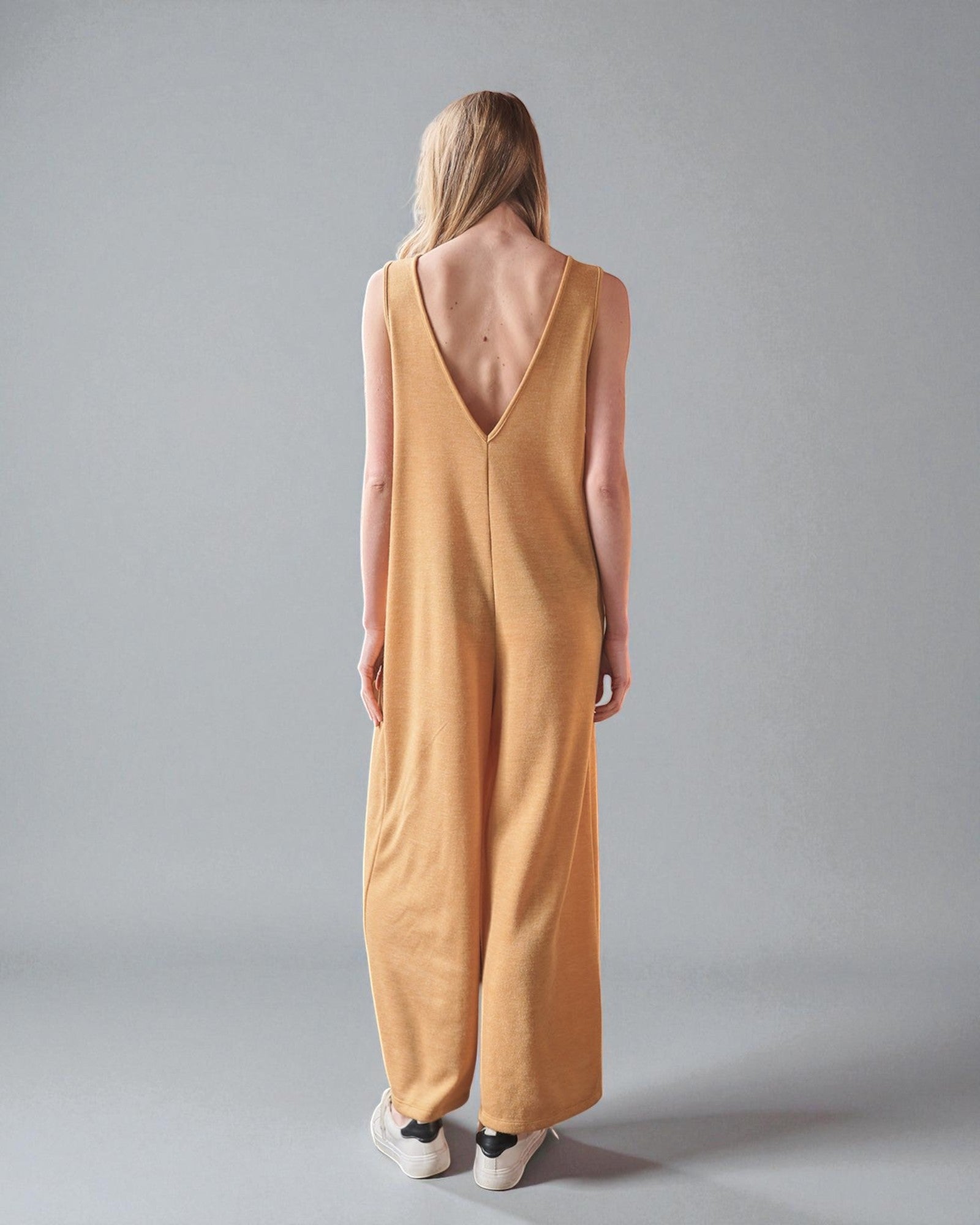 Woman wearing a mustard yellow dress with a deep V-neck on a gray background