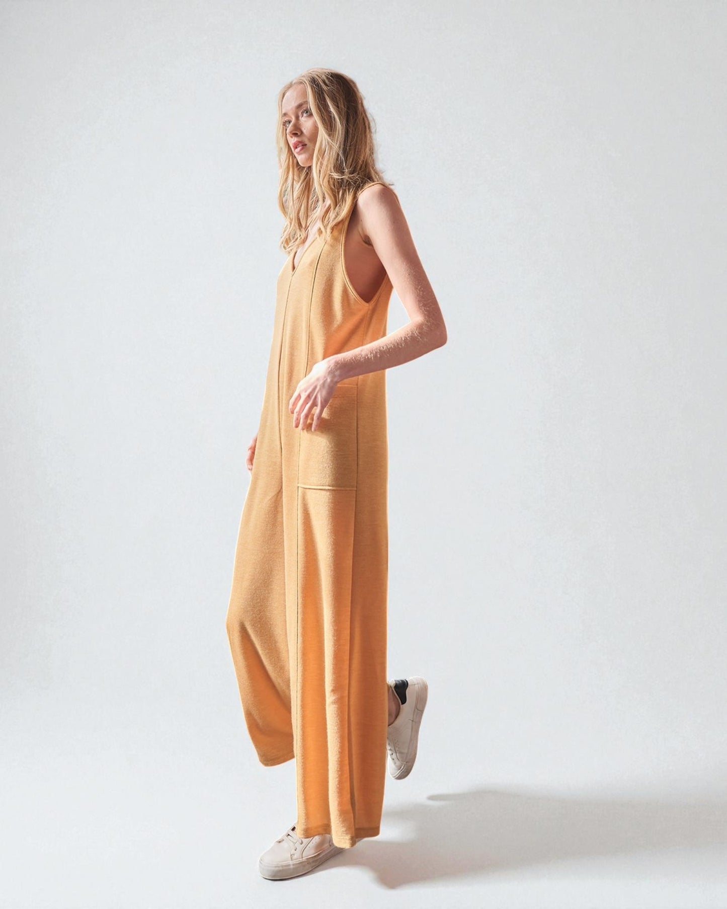 Woman wearing a mustard yellow sleeveless jumpsuit on a white background