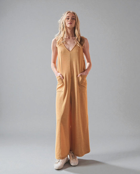 Woman wearing a mustard yellow jumpsuit against a gray background