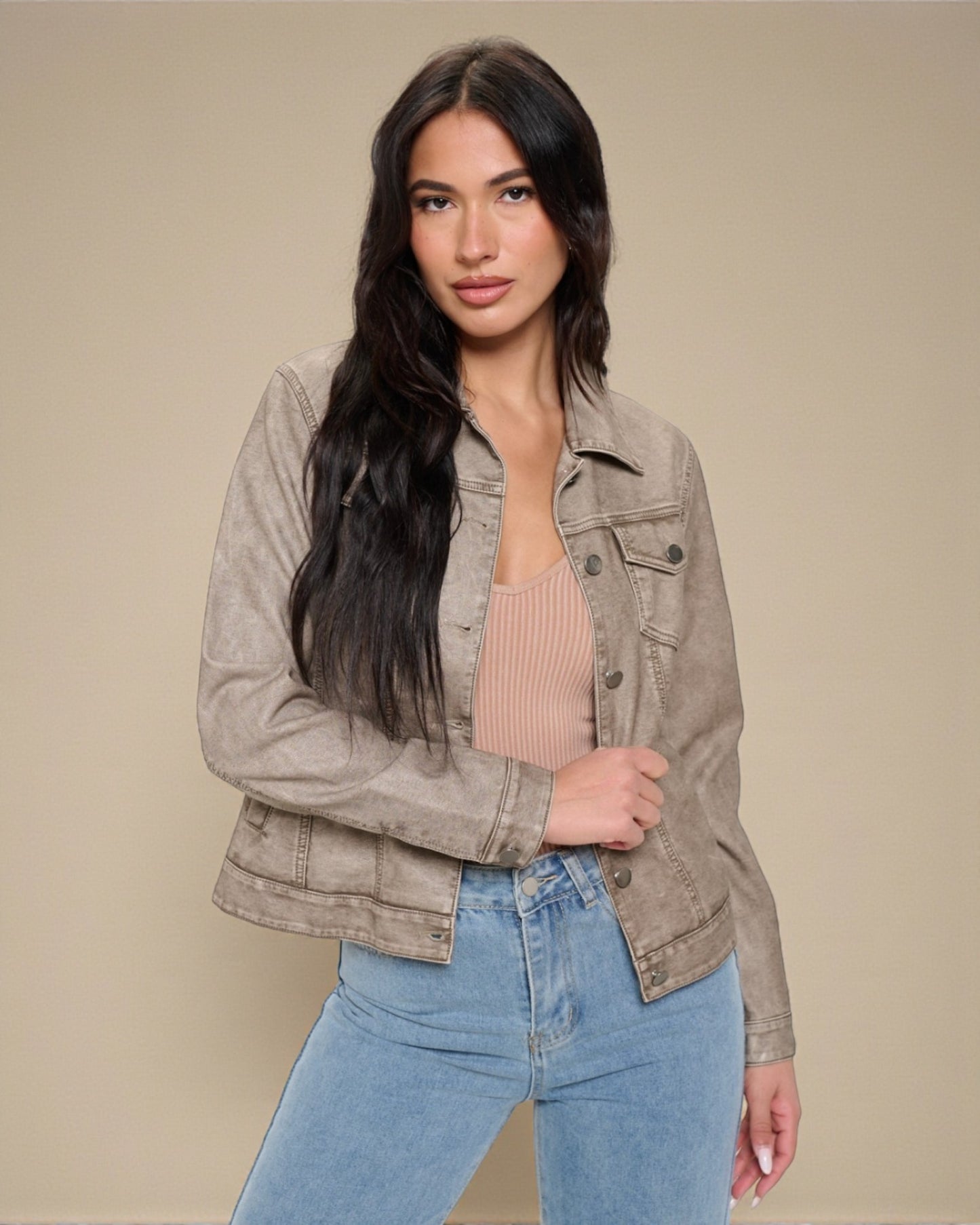 Woman wearing a beige jacket and blue jeans against a beige background