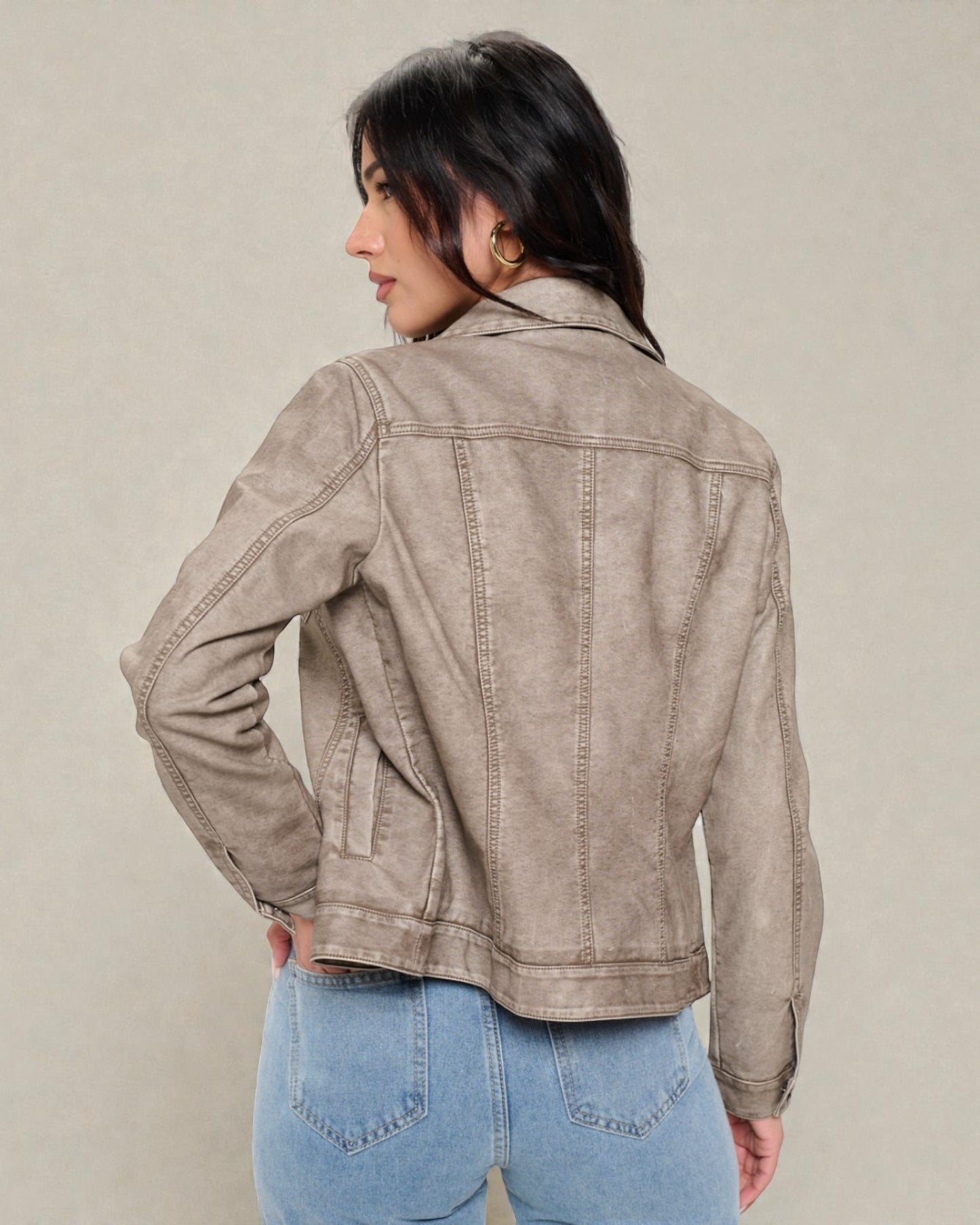 Woman wearing a beige denim jacket and blue jeans against a plain background